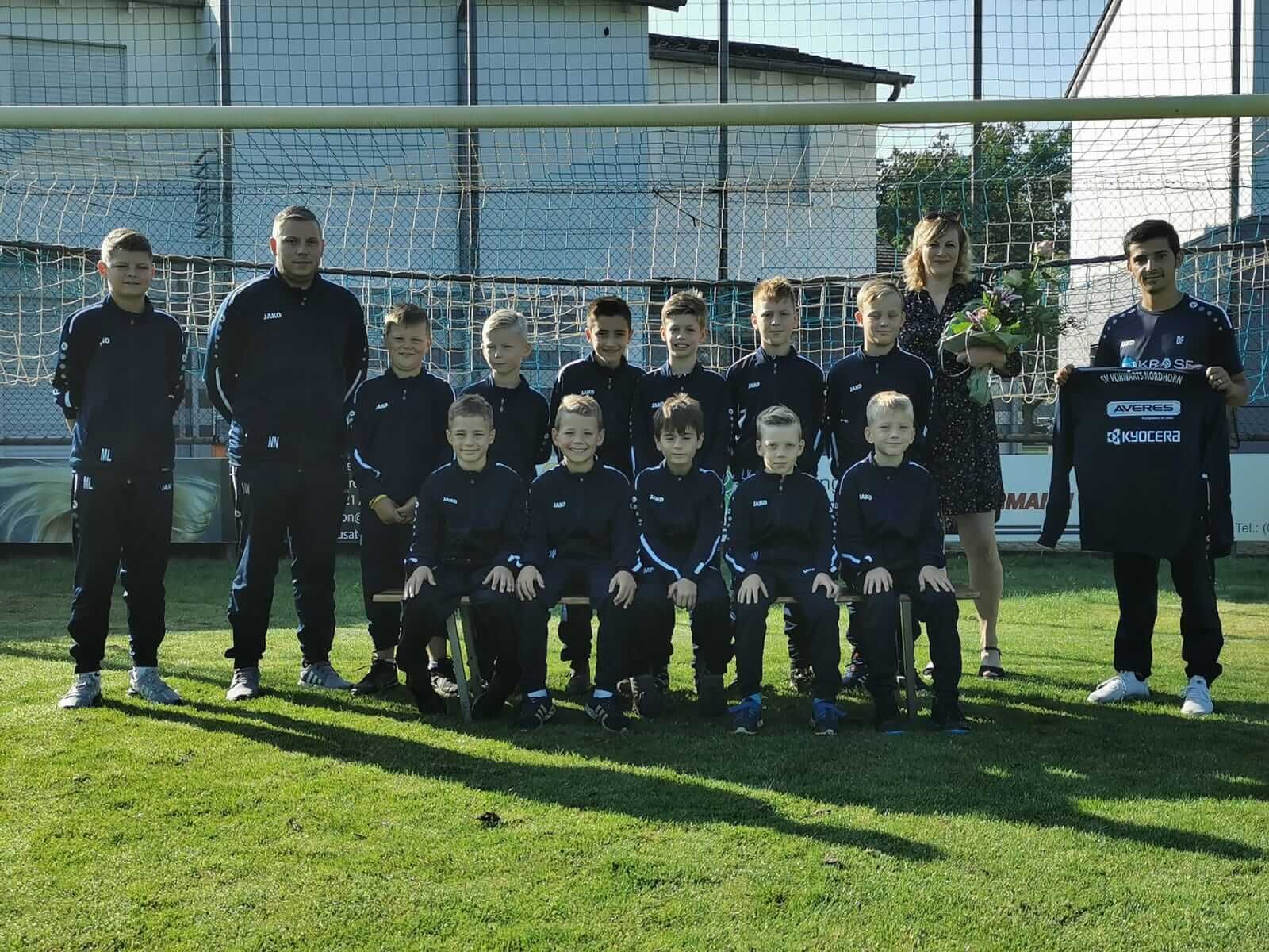 Mannschaftsfoto der Minikicker SV Vorwärts Nordhorn auf Spielfeld mit Tor im Hintergrund, Neues Trikot der Spendenübergabe wird gezeigt.